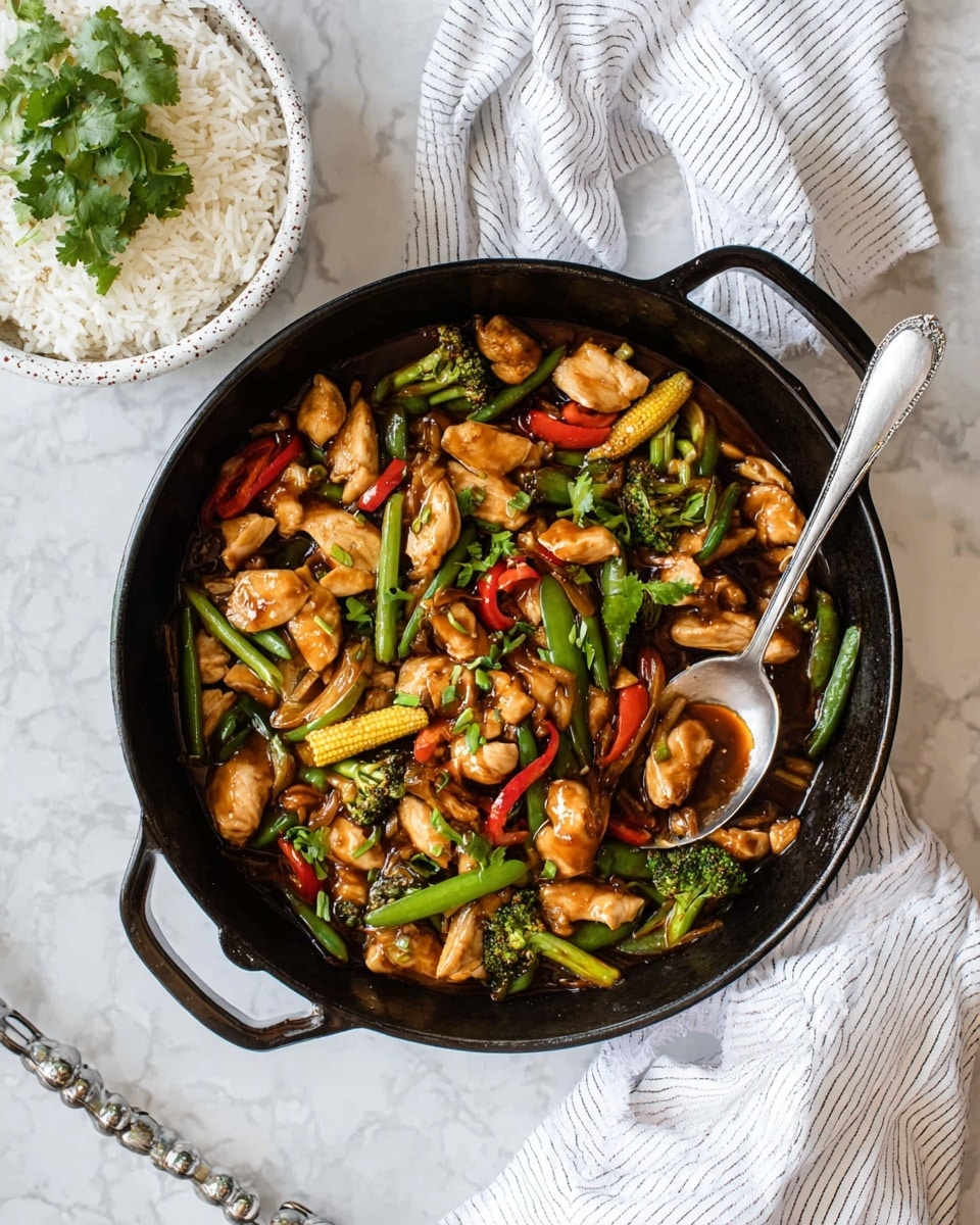 A round black cast iron pan filled with a colorful stir-fry sits on a white marbled surface, showing about three main layers: tender chunks of light brown chicken scattered evenly, mixed with bright green snap peas, light yellow baby corn, dark green broccoli, red cherry tomatoes, thin red chili strips, and beige onion pieces. The stir-fry has a glossy, dark brown sauce coating the ingredients, with a silver spoon resting inside the pan. To the left, there is a white speckled bowl filled with white rice topped with fresh green cilantro leaves, and below the pan is a white striped cloth with a metal handle peeking out. photo taken with an iphone --ar 4:5 --v 7