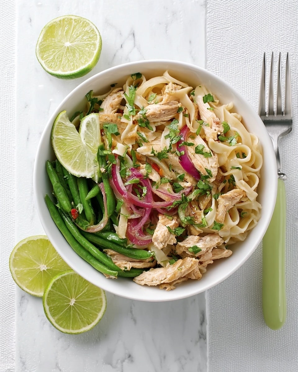 A white bowl filled with three layers of food: the bottom layer is flat white noodles, mixed with thin green beans; the middle layer has strips of cooked chicken and some red onion slices; the top layer is sprinkled with chopped green herbs. Half a lime sits on the edge of the bowl, and a slice of lime is placed nearby on a white marbled surface. A fork with a pale green handle rests beside the bowl. photo taken with an iphone --ar 4:5 --v 7