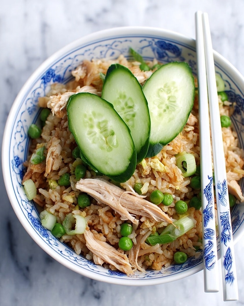 A white bowl with blue patterns holds a layer of light brown fried rice mixed with green peas and chopped green onions. On top of the rice, there are several pieces of shredded cooked chicken and three slices of fresh cucumber placed near the center. Two pairs of white chopsticks with blue designs rest on the side of the bowl. The bowl is placed on a white marbled surface. Photo taken with an iphone --ar 4:5 --v 7