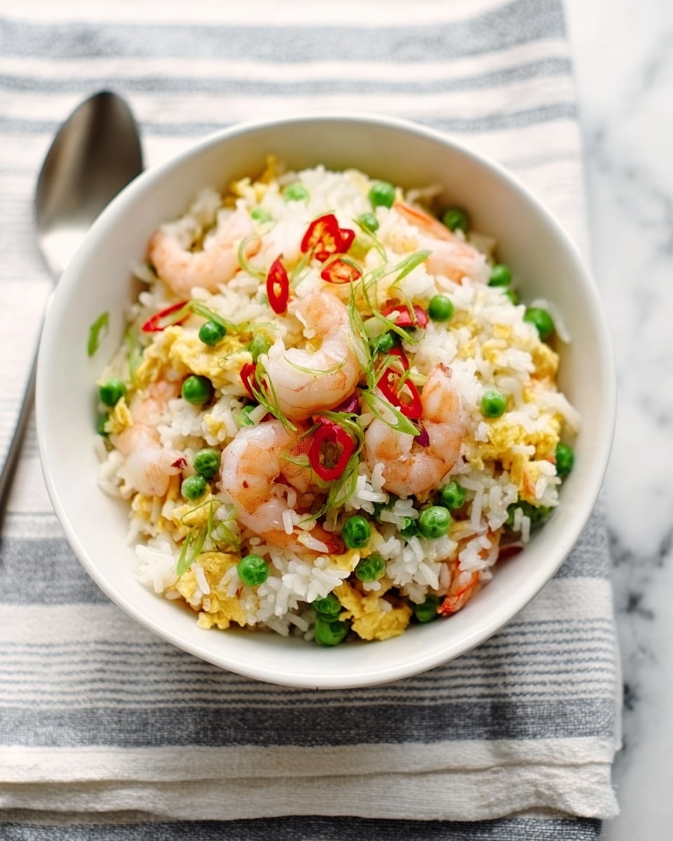 A white bowl filled with a colorful shrimp fried rice dish is placed on a striped cloth with a white marbled texture surface beneath. The dish has a layer of fluffy white rice mixed evenly with bright green peas and small pieces of yellow scrambled egg, scattered throughout. On top, there are pink shrimp pieces that sit above the rice, adding a slightly rough texture. Thin slices of red chili and green herbs are sprinkled over the shrimp, adding pops of color and a fresh look. The bowl has a simple silver spoon placed beside it on the cloth. Photo taken with an iphone --ar 4:5 --v 7