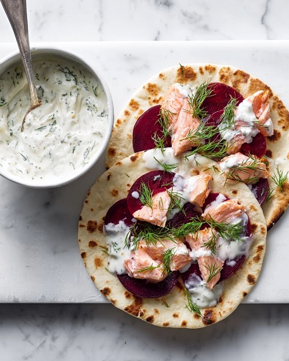 A white flatbread sits on a white marbled surface with circular light brown toasted spots. On top, another flatbread is layered with thin dark red beet slices spread evenly, followed by pieces of light pink cooked salmon scattered on top. White creamy sauce is drizzled over the salmon, and delicate green dill sprigs are placed as garnish. To the left, a white bowl filled with creamy herb sauce has a silver spoon resting inside. Photo taken with an iphone --ar 4:5 --v 7
