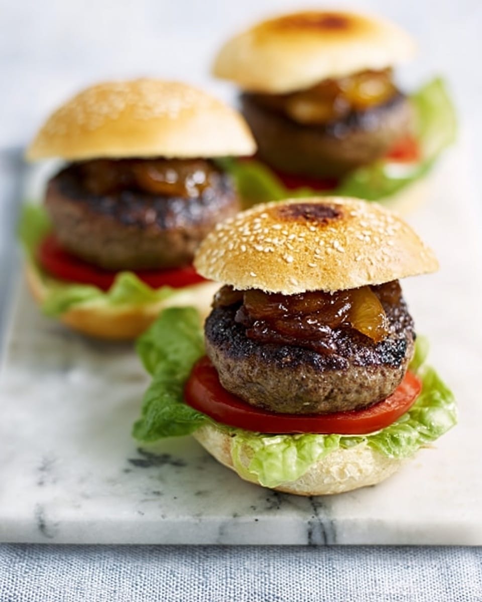 Two open white sesame seed buns each hold a small hamburger. Each burger has a dark brown grilled patty placed on a slice of red tomato and green leafy lettuce, with a glossy caramelized onion topping on the patty. One bun top is placed nearby showing its toasted golden brown inside, and the other bun top is in the background also toasted but upside down. The setup is on a white marbled surface with a light cloth underneath. photo taken with an iphone --ar 4:5 --v 7