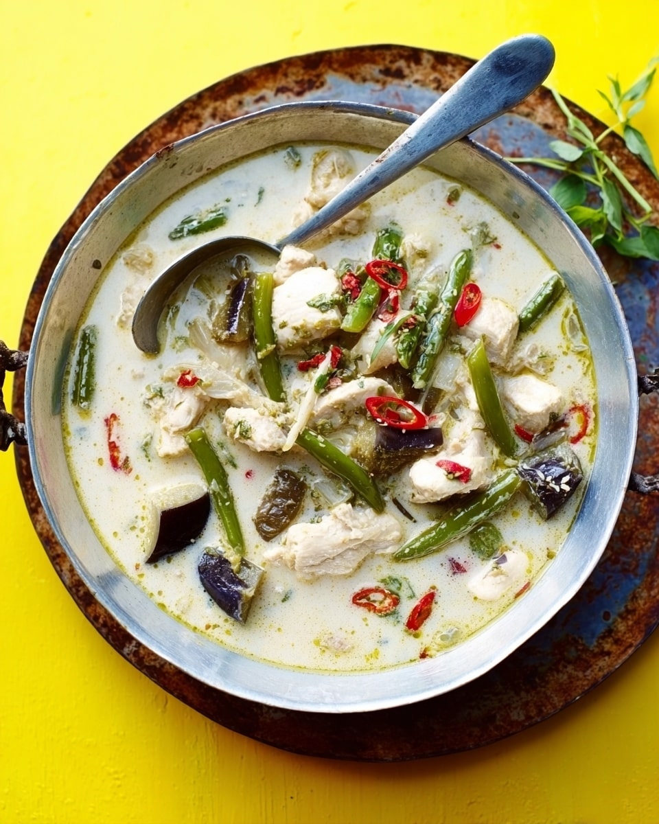 The image shows a round, silver metal pan filled with a creamy white soup that has chunks of white chicken, green beans, and pieces of dark eggplant floating on top. The soup has small red chili slices scattered across the surface. The pan rests on a worn, round, rusty brown tray, placed on a bright yellow background. A large silver spoon is inside the pan, angled slightly to the right. In the upper right corner, green herbs peek out, and a woman's hand holds the pan’s handle on the left side. The photo taken with an iphone --ar 4:5 --v 7