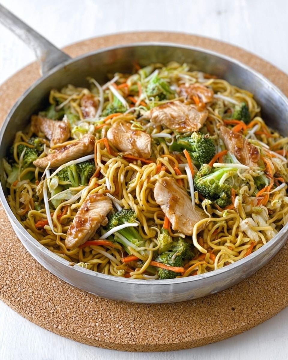 A large metal pan filled with stir-fried noodles and vegetables. The bottom layer shows yellowish noodles twisted and mixed. On top of the noodles are several pieces of cooked chicken with a light brown glaze. Around and above the chicken are small green broccoli florets and thin white bean sprouts. Thin orange carrot strips and small bits of light green vegetables are scattered throughout. The pan sits on a natural cork mat on a white marbled surface with a neutral background. Photo taken with an iphone --ar 4:5 --v 7