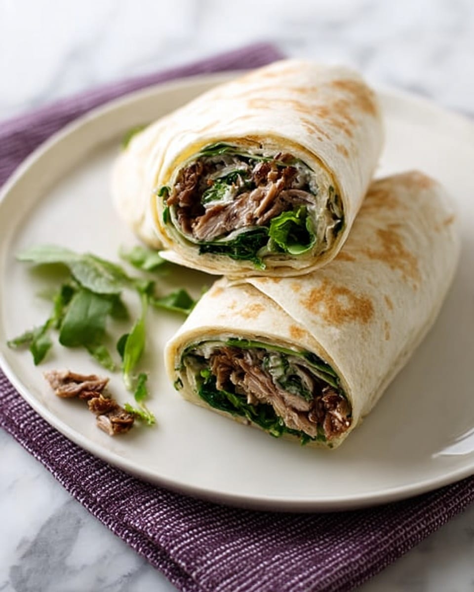 Two wraps are placed on a white plate over a folded purple cloth, all set on a white marbled surface. Each wrap is cut in half and stacked, showing three layers inside: a light beige soft tortilla on the outside, a filling of cooked, shredded brown meat in the middle, and fresh green leafy vegetables inside. Small green leaves and a few meat bits are scattered on the plate beside the wraps. Photo taken with an iphone --ar 4:5 --v 7