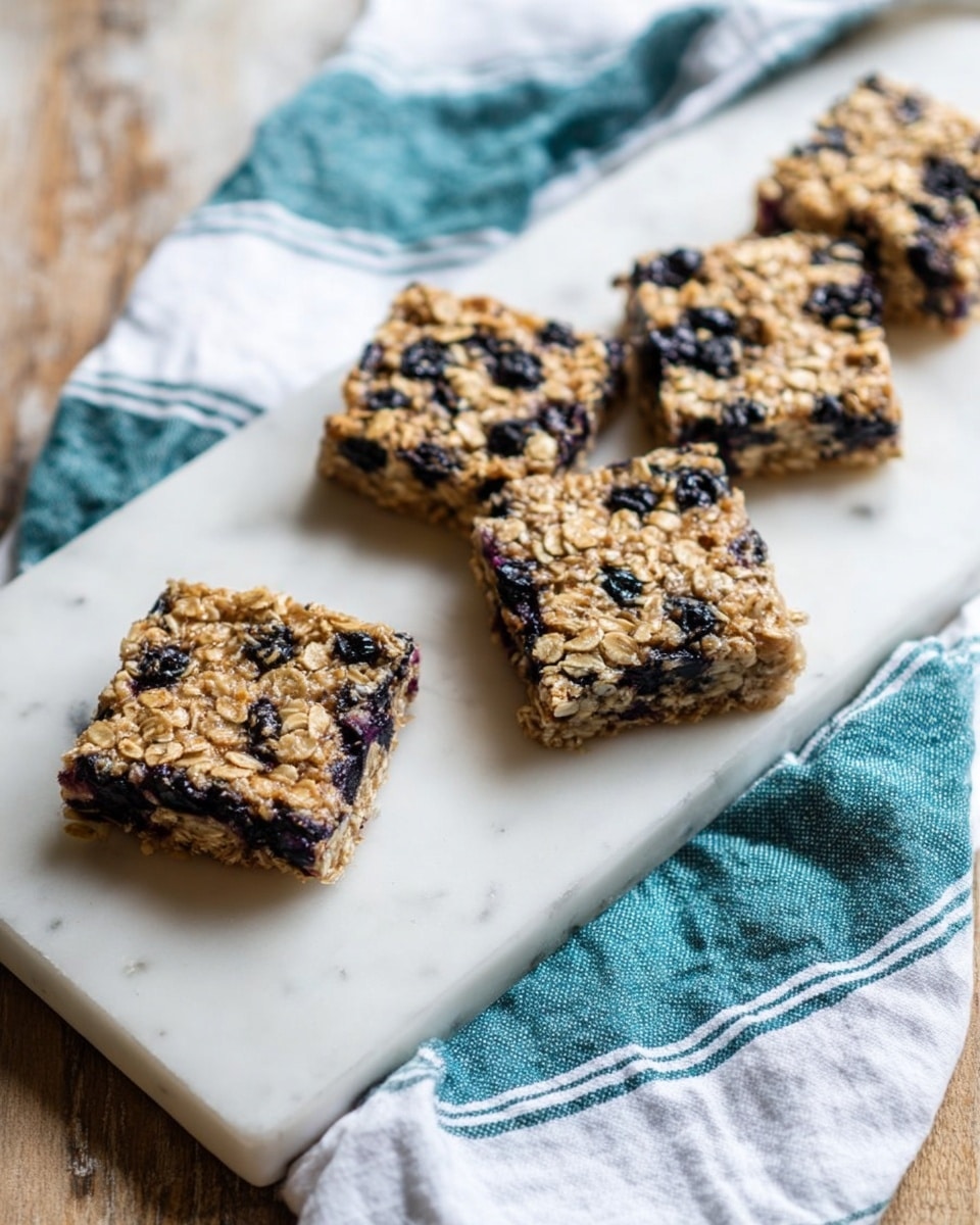 Four square oat bars with visible blueberries scattered through them sit in a single line on a white marble rectangular board. The oat bars are light brown with a rough, crumbly texture and dark purple spots from the blueberries. The marble board rests on a white cloth with blue-green stripes and fringed edges, all placed on a rustic wooden surface. Photo taken with an iphone --ar 4:5 --v 7
