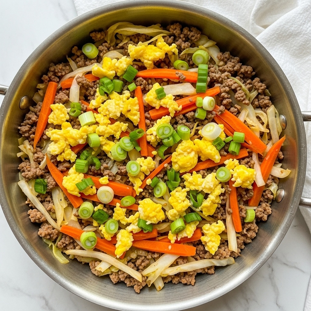 A large silver pan filled with a mix of cooked ground meat, thinly sliced light green cabbage, small chunks of yellow scrambled eggs, and small pieces of bright orange carrots, all mixed evenly together. The dish is garnished with fresh thinly sliced green onions scattered on top. The pan sits on a white marbled surface, with some green onions visible next to it. The textures contrast between the soft scrambled eggs, tender meat, and crisp vegetables. photo taken with an iphone --ar 4:5 --v 7