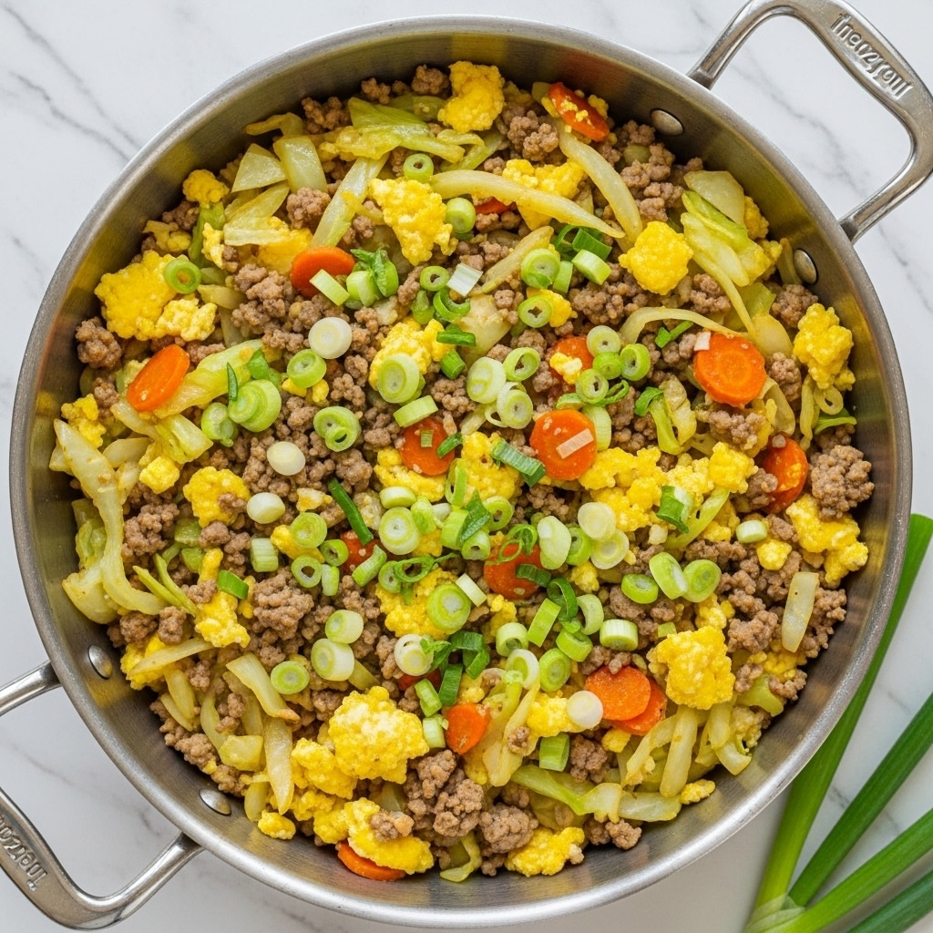 The image shows a metal pan full of cooked food with several layers mixed together. The base layer is brown cooked ground meat, interspersed with thin white and light green strips of cabbage. Bright orange carrot pieces and fluffy yellow scrambled egg bits are scattered on top, adding vibrant color. Sliced green onions are sprinkled evenly over the dish, providing fresh green notes. The pan is placed on a white marbled surface, and a white cloth is partially visible in the background. Photo taken with an iphone --ar 4:5 --v 7