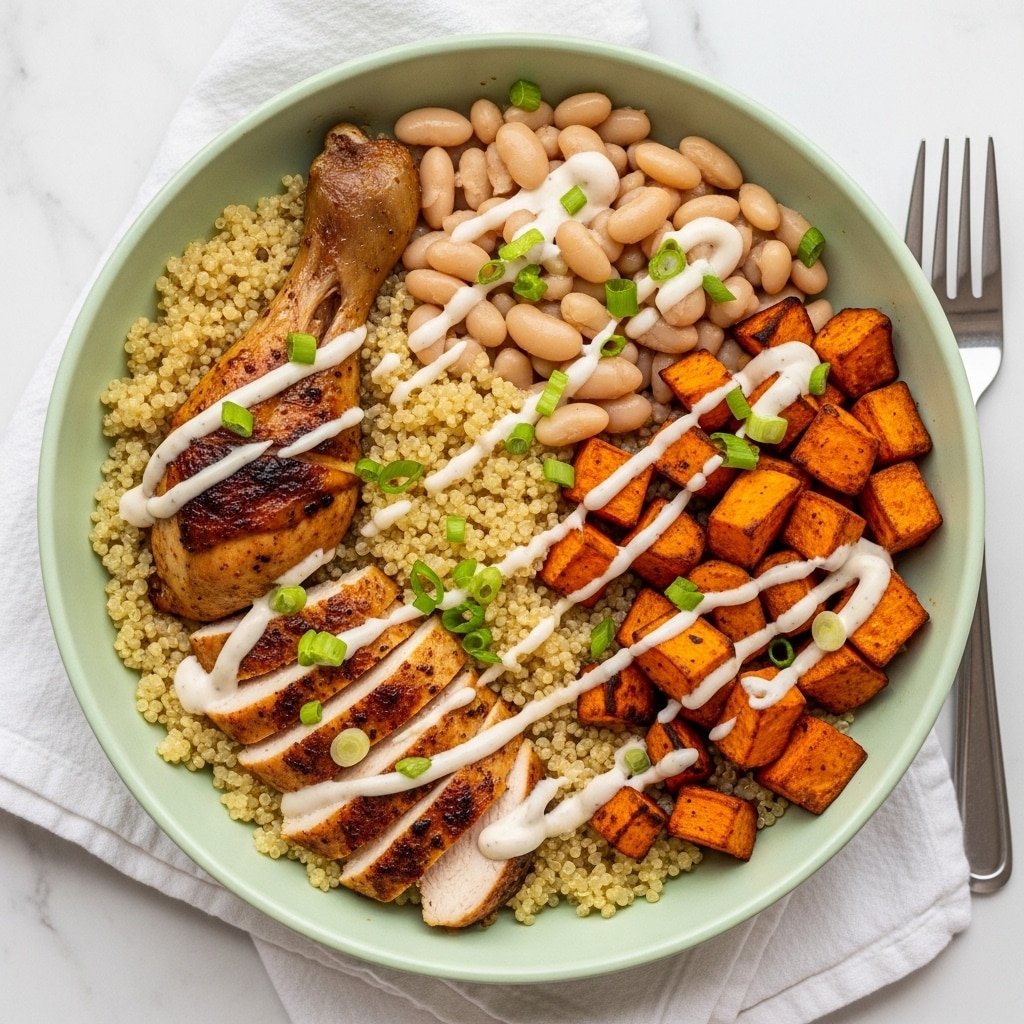 A green bowl filled with a base layer of yellow quinoa, topped with three sections: roasted sweet potato cubes with a slightly charred look on the left, pale white cooked beans on the right, and a browned chicken drumstick along with sliced chicken pieces at the top. The ingredients are lightly drizzled with a creamy white sauce and garnished with green chopped scallions. The bowl sits on a white cloth next to a silver fork, all placed on a white marbled surface. photo taken with an iphone --ar 4:5 --v 7
