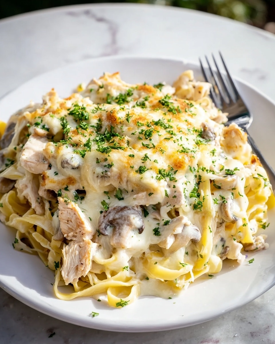 A white plate holds a layered pasta dish with thick, flat noodles forming the bottom layer, pale yellow and soft in texture. On top of the pasta are pieces of light beige cooked chicken and slices of mushrooms. The whole dish is covered with a creamy white sauce that looks rich and smooth, topped with melted, slightly browned cheese that adds a golden touch in spots. Bright green chopped parsley is sprinkled over the top, adding fresh color and contrast. A fork rests on the side of the plate, and the setting is on a white marbled surface. photo taken with an iphone --ar 4:5 --v 7