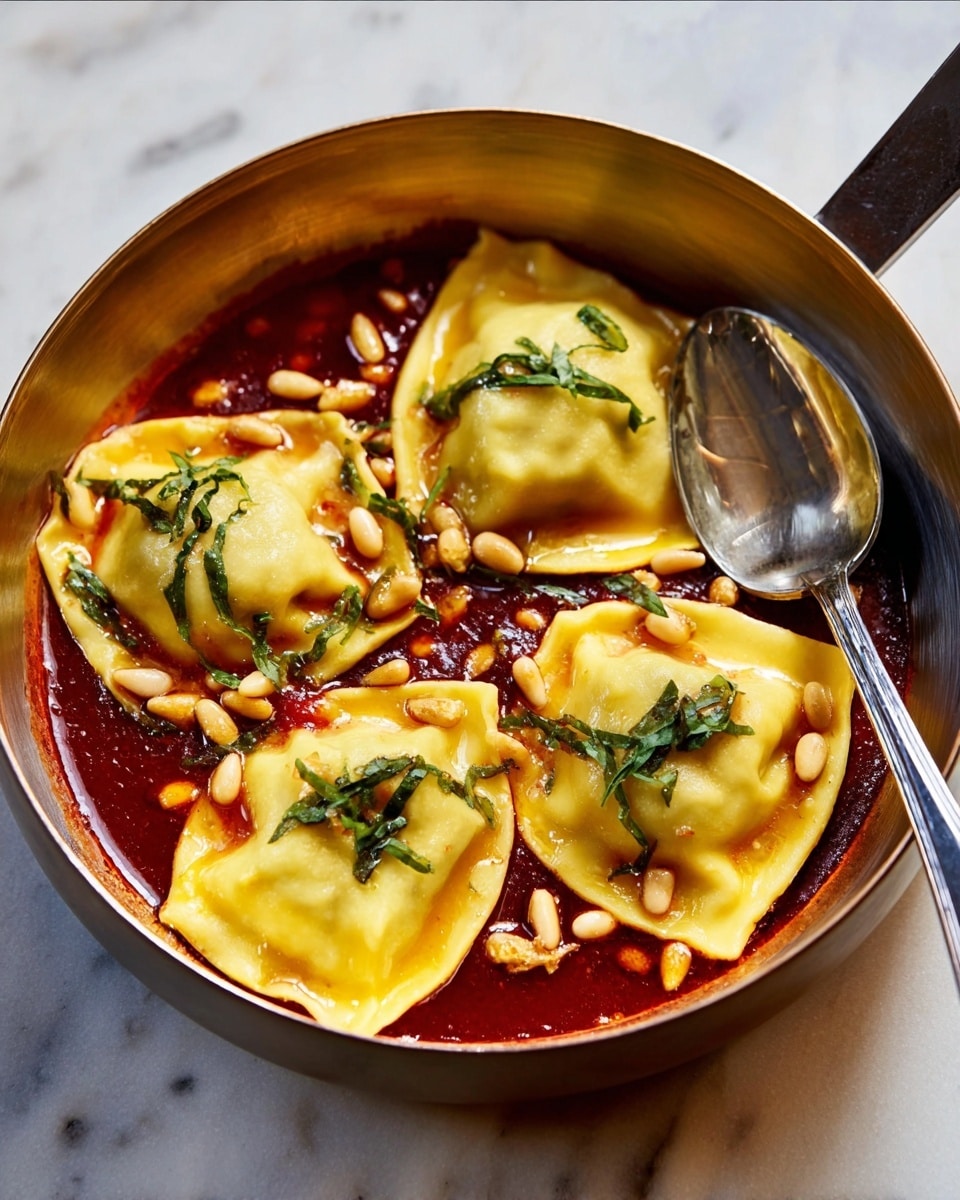 A round white bowl holds five yellow, soft ravioli dumplings floating in a thick bright red tomato sauce. The sauce has a smooth texture with visible shiny oil spots on top. Small pine nuts are scattered over the sauce and ravioli, along with tiny green herb leaves adding a fresh touch. The bowl is placed on a white marbled surface with soft natural light highlighting the colors and textures. Photo taken with an iphone --ar 4:5 --v 7