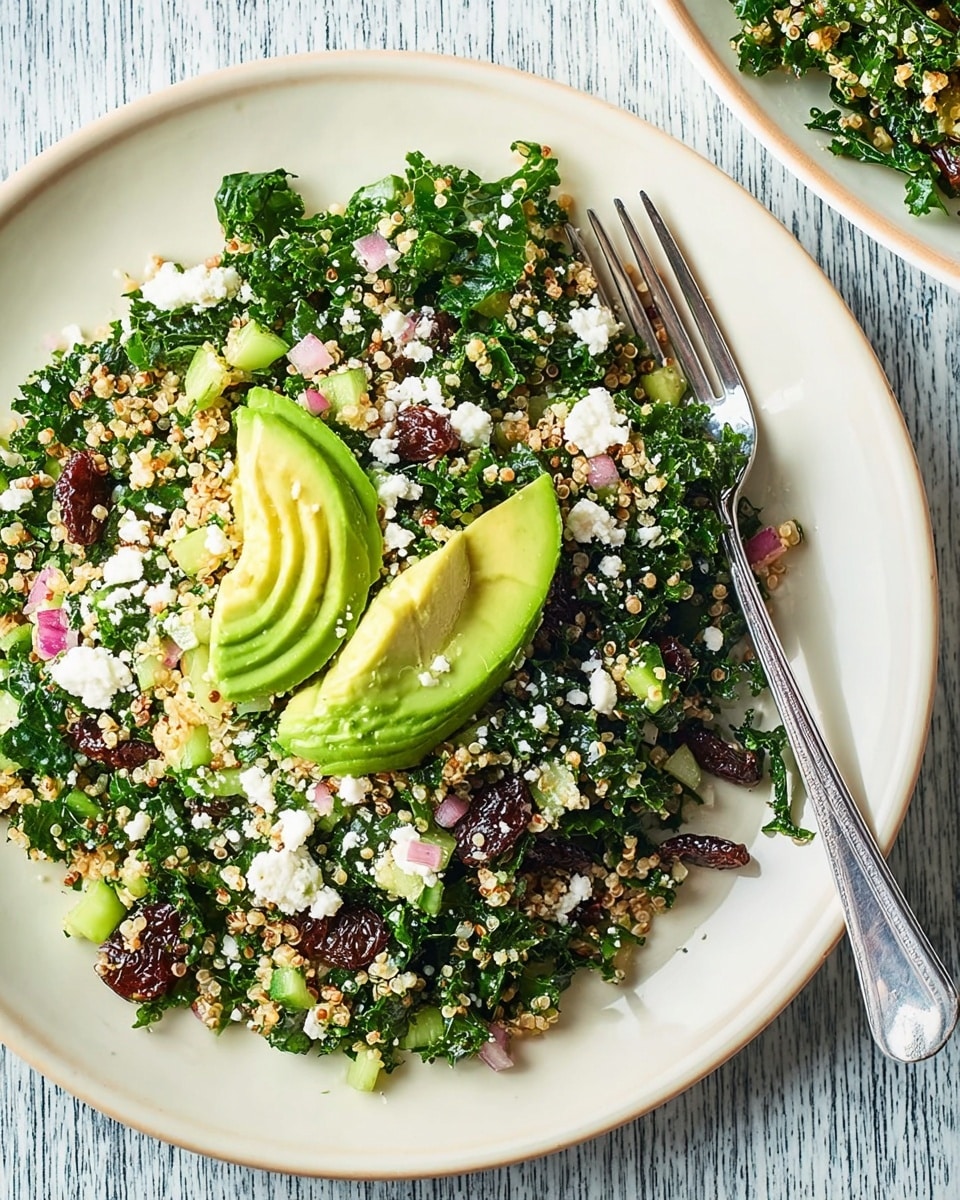 Two white round plates sit on a white marbled textured surface. The main plate at the center shows a salad base made of chopped dark green kale mixed with small bits of red onion, green celery, tiny beige quinoa grains, and dark brown raisins scattered throughout. On top of this colorful salad layer are several slices of bright green avocado, thinly sliced and fanned out. White crumbles of cheese are sprinkled over the avocado and salad. A silver fork rests on the right side of the main plate. Part of another white plate with the same salad and avocado arrangement is visible on the left side with a silver fork placed on top. The light is bright and natural, highlighting the fresh textures of the ingredients. Photo taken with an iphone --ar 4:5 --v 7