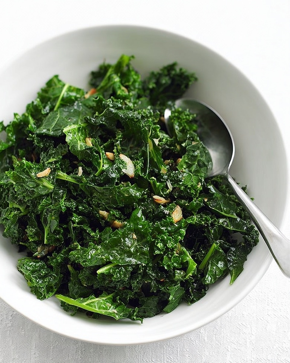 A white bowl filled with cooked kale and chopped garlic pieces, showing dark green leafy texture mixed with lighter green bits. A silver spoon rests inside the bowl to the right side. The background and surface are white marbled texture. photo taken with an iphone --ar 4:5 --v 7