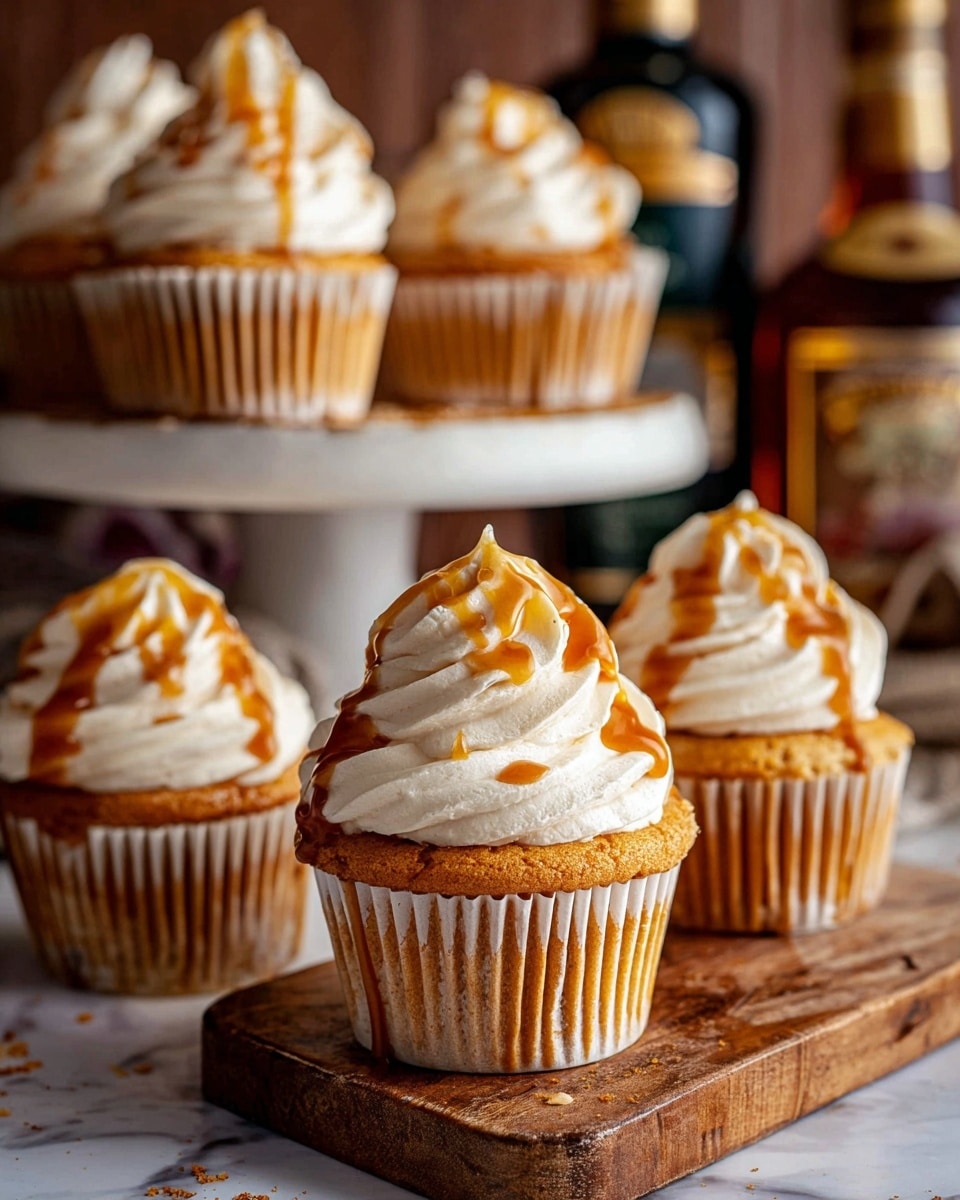 The image shows several golden brown cupcakes with a light, fluffy texture, each wrapped in a white paper liner with vertical ridges. Each cupcake is topped with a generous swirl of smooth, creamy off-white frosting, which forms elegant, tall peaks. Drizzled over the frosting is a shiny caramel sauce that adds a rich amber color and glossy finish, creating a contrast with the soft frosting. The cupcakes are placed on a light wooden board with visible grain and slight grooves, set against a white marbled surface. Behind the cupcakes, blurred bottles and other kitchen items add depth to the cozy setting. Photo taken with an iphone --ar 4:5 --v 7