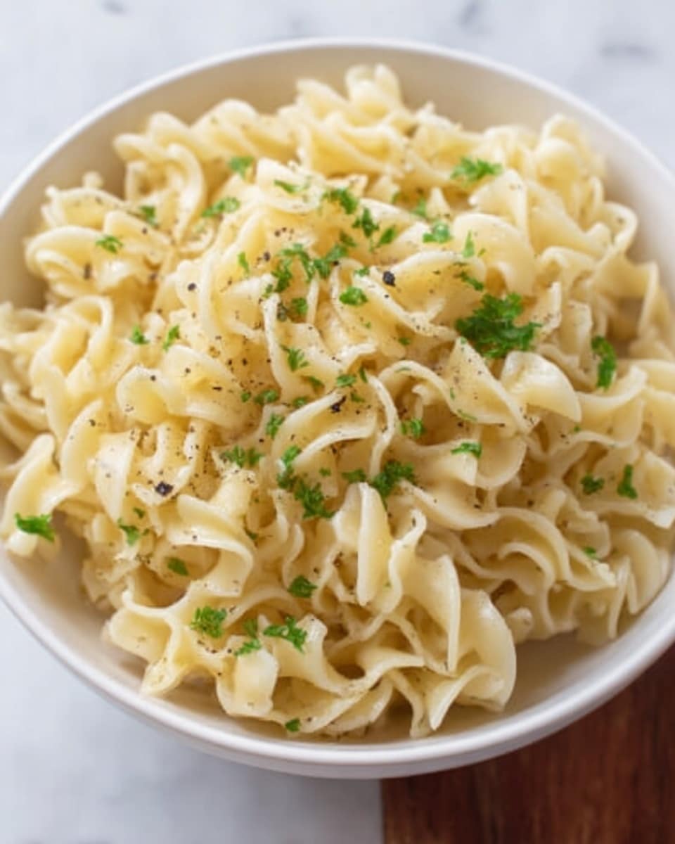 A white bowl holds a generous serving of curly pasta shaped like corkscrews, light yellow in color with a slightly glossy texture. On top, small green parsley leaves are scattered evenly, adding fresh color and contrast. The pasta looks soft and cooked just right, sitting on a white marbled surface. Photo taken with an iphone --ar 4:5 --v 7