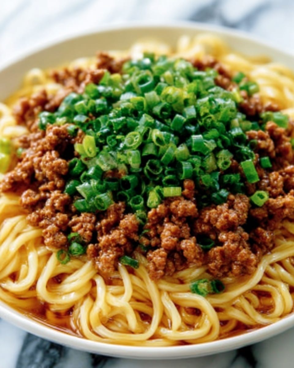A close-up image of a white bowl filled with thick, curly yellow noodles as the base layer, topped generously with small pieces of cooked brown minced meat and bright green chopped scallions spread evenly on top, creating a colorful contrast. The noodles look glossy with a slight sauce coating, and the minced meat has a crumbly texture while the scallions add freshness. The bowl sits on a white marbled surface. photo taken with an iphone --ar 4:5 --v 7